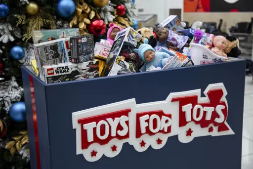 A Toys for Tots donation bin in front of a Christmas tree